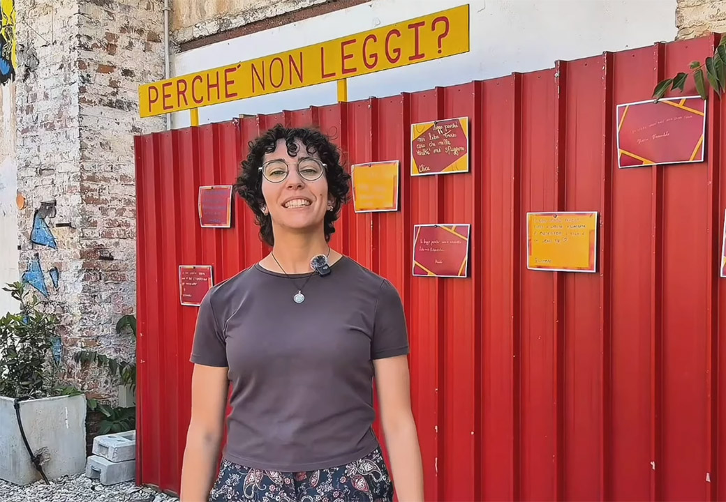 Una donna davanti ad un muro con la scritta "Perché non leggi?"
