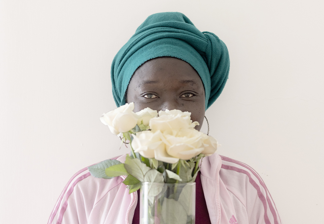 Una donna nera tiene un vaso di fiori bianchi davanti al viso