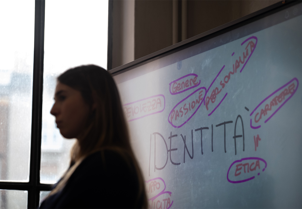 Una ragazza con alle spalle una lavagna che riporta diverse parole legate a "identità"