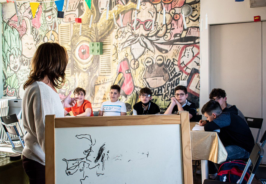 Ragazzi seduti ai banchi in un aula con un murales colorato