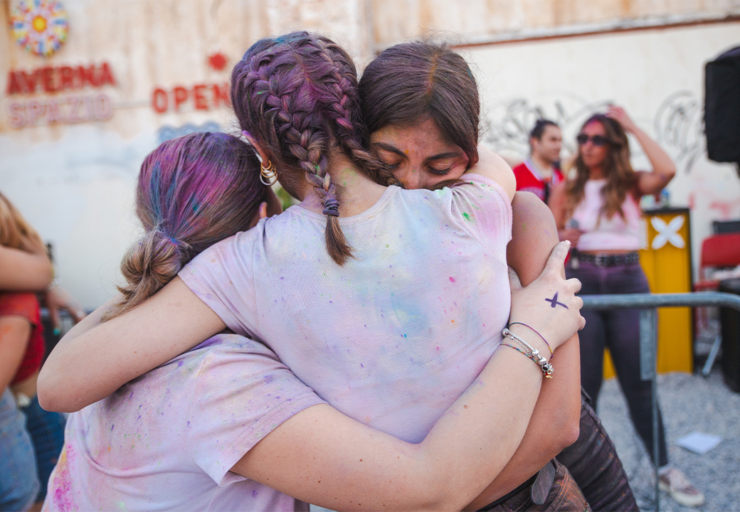 Tre ragazze ricoperte da una polvere colorata si abbracciano