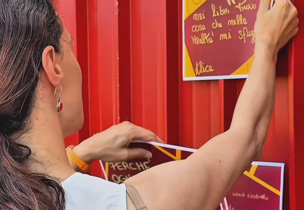 Una donna appende dei fogli scritti a mano su un muro rosso